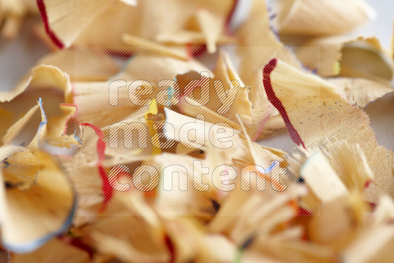 A close-up showing a small pile of pencil shavings with varied color edges on grey background