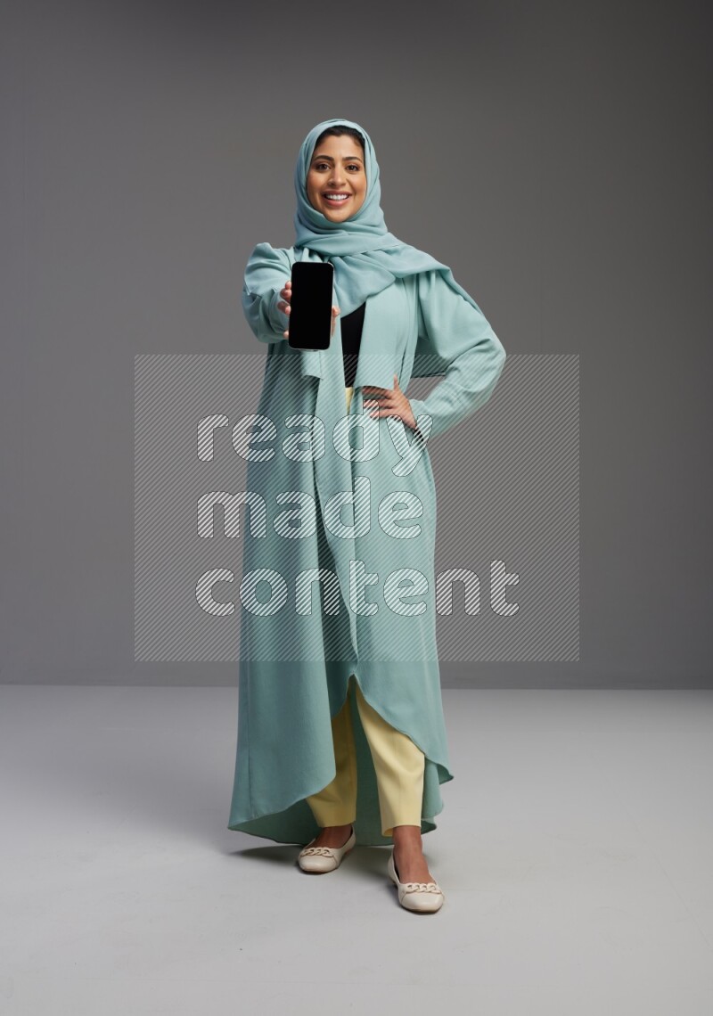 Saudi Woman wearing Abaya standing showing phone to camera on Gray background