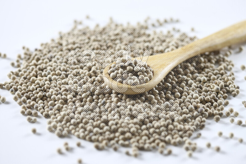 حبوب الفلفل الأبيض مع ملعقة خشبية علي خلفية بيضاء