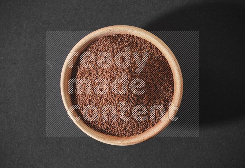A wooden bowl full of garden cress seeds on a black flooring