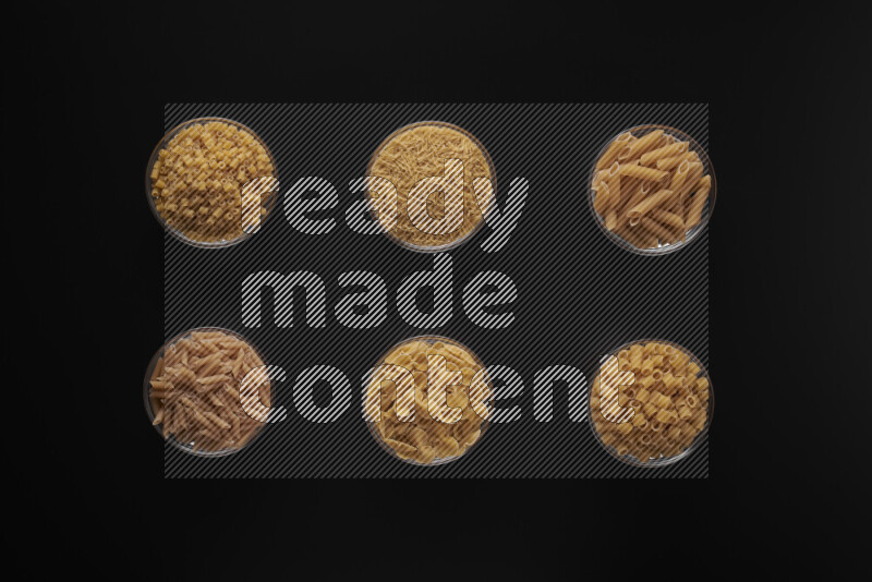Different pasta types in 6 glass bowls on black background