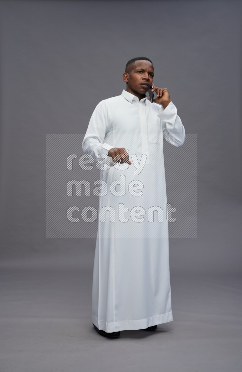 Saudi man wearing thob standing talking on phone on gray background