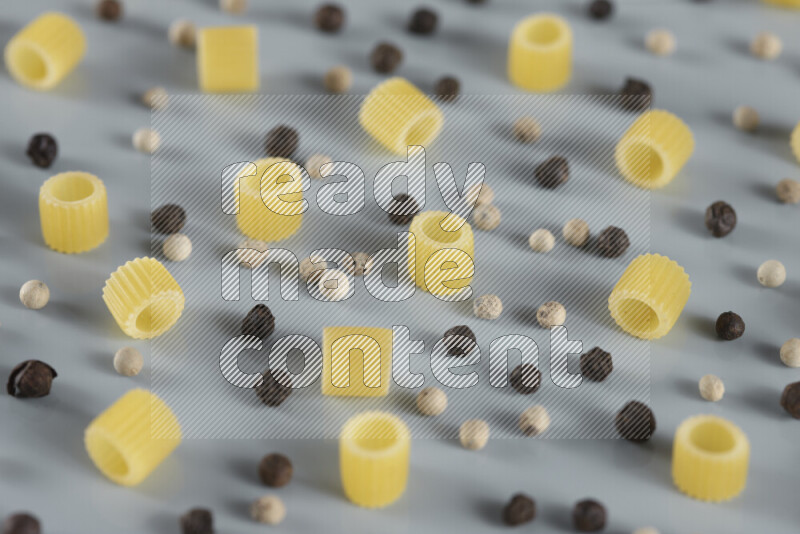 Raw pasta with different ingredients such as cherry tomatoes, garlic, onions, red chilis, black pepper, white pepper, bay laurel leaves, rosemary, cardamom and mushrooms on light blue background