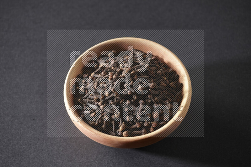 A wooden bowl full of cloves on a black flooring