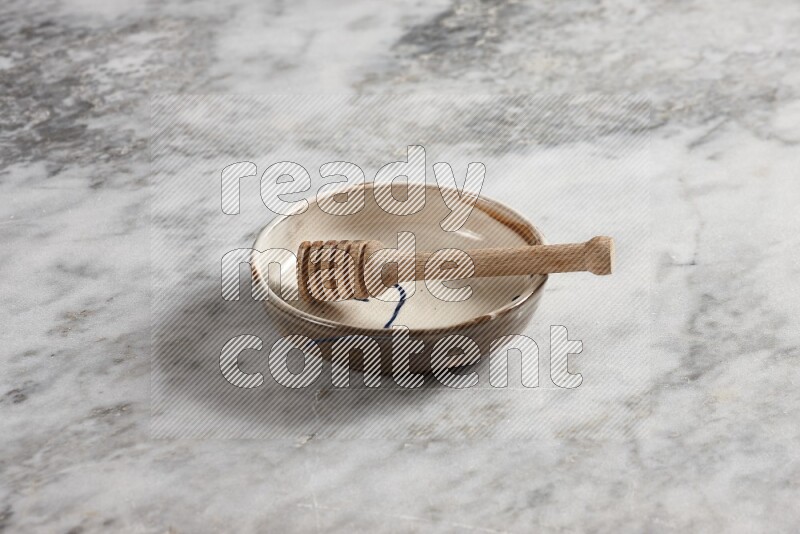 Multicolored pottery bowl with wooden honey dipper in it on grey marble background