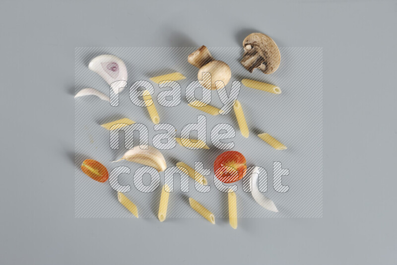 Raw pasta with different ingredients such as cherry tomatoes, garlic, onions, red chilis, black pepper, white pepper, bay laurel leaves, rosemary, cardamom and mushrooms on light blue background