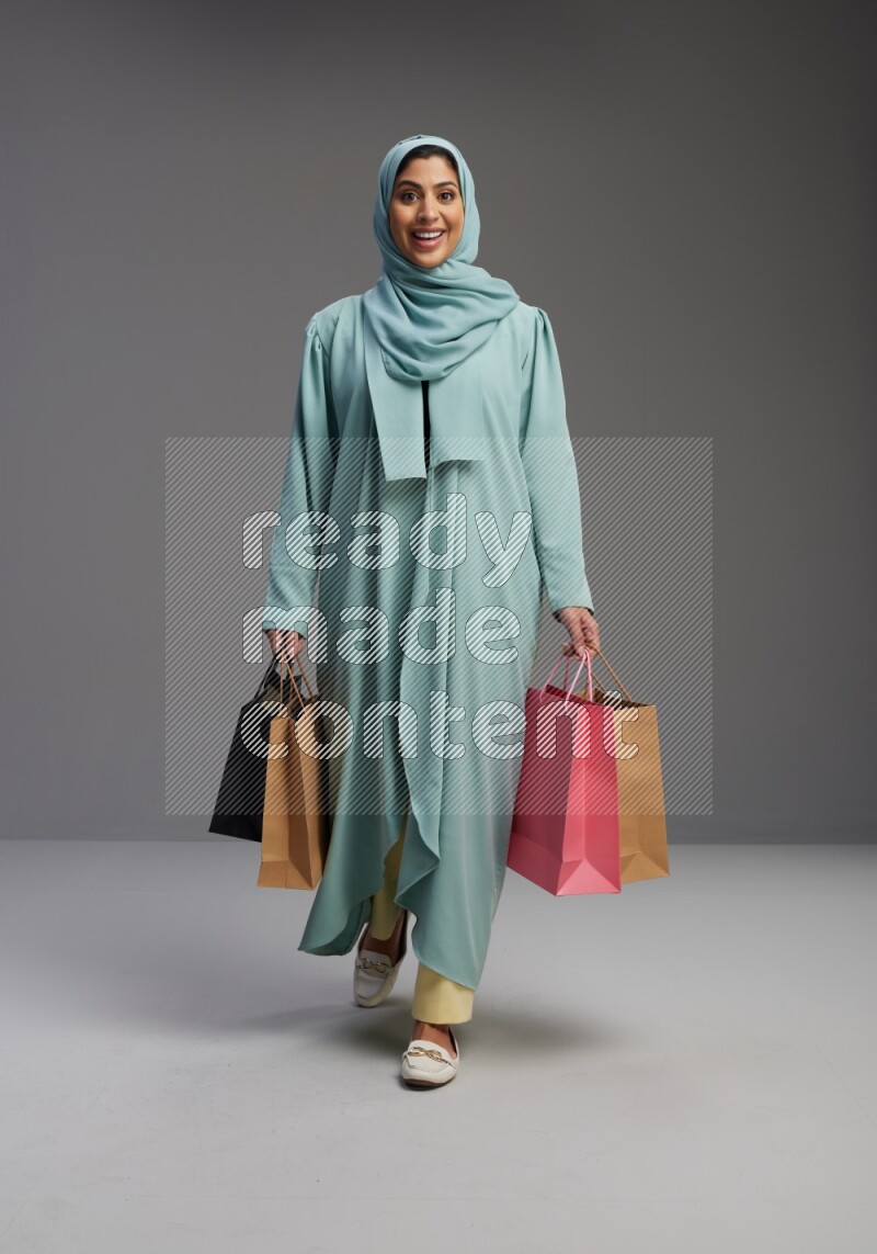 Saudi Woman wearing Abaya standing holding shopping bag on Gray background