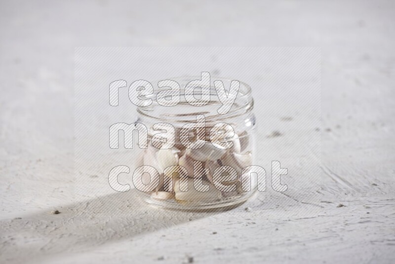 A glass jar full of garlic cloves on a textured white flooring
