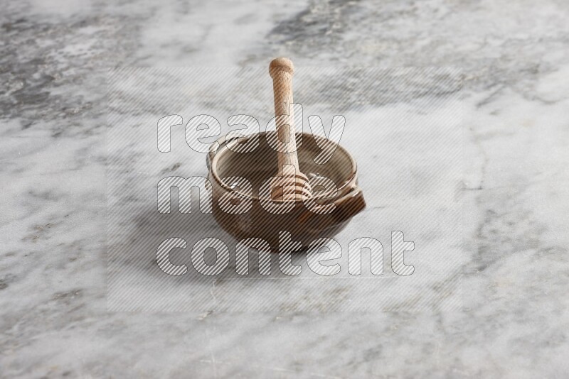 Multicolored pottery bowl with wooden honey dipper in it on grey marble background