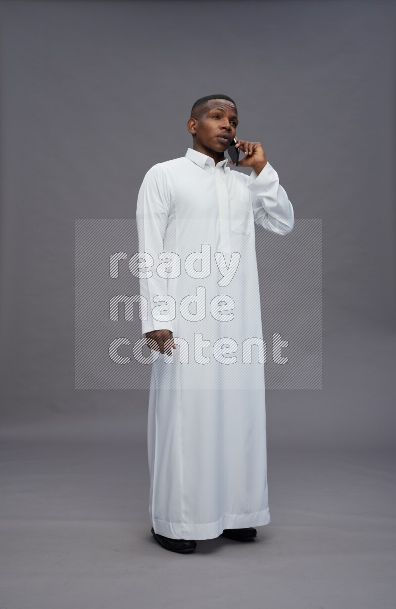 Saudi man wearing thob standing talking on phone on gray background