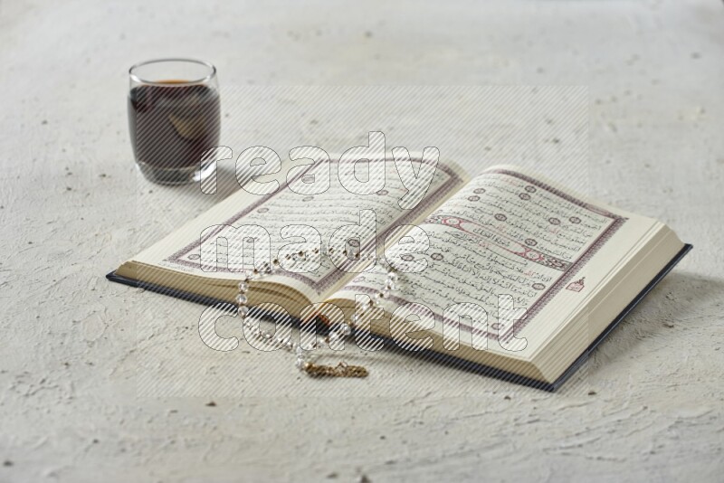 Quran with dates, prayer beads and different drinks all placed on textured white background