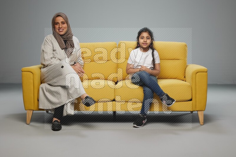 A girl with her mother sitting and interacting with the camera on gray background
