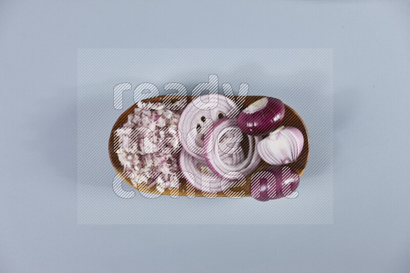 A close-up shot of red onions displayed in different forms including whole, sliced into rings, and finely chopped arranged on a wooden plate on light blue background
