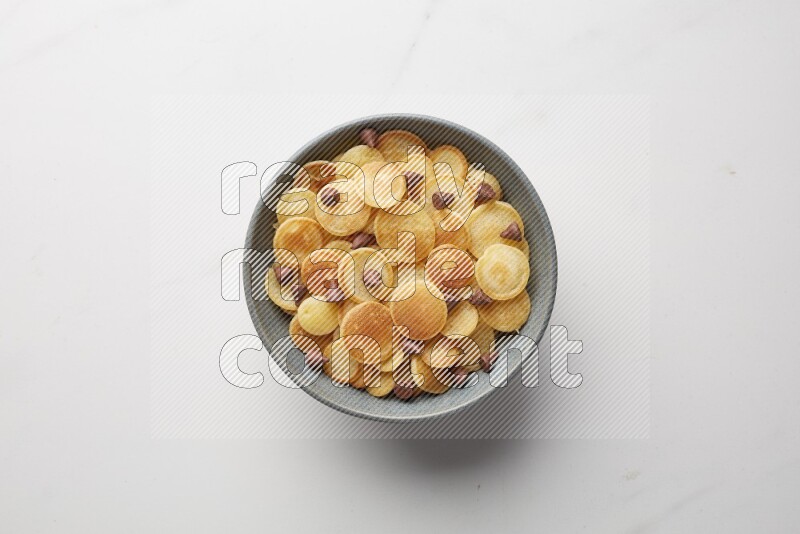Top-view shot of chocolate chips cereal pancakes in a round bowl on white background