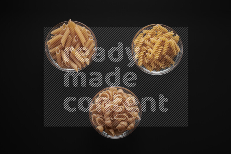 Different pasta types in glass bowls on black background
