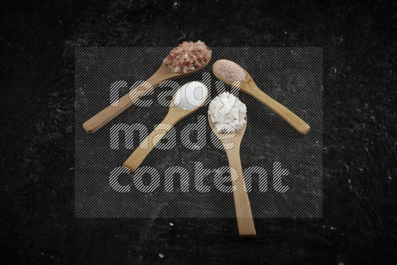 4 wooden spoons filled with fine and coarse salt on black background