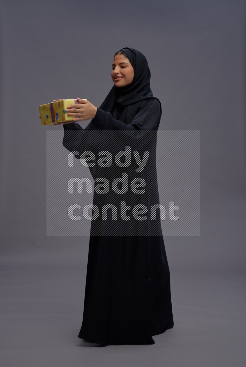 Saudi woman wearing Abaya standing holding gift box on gray background