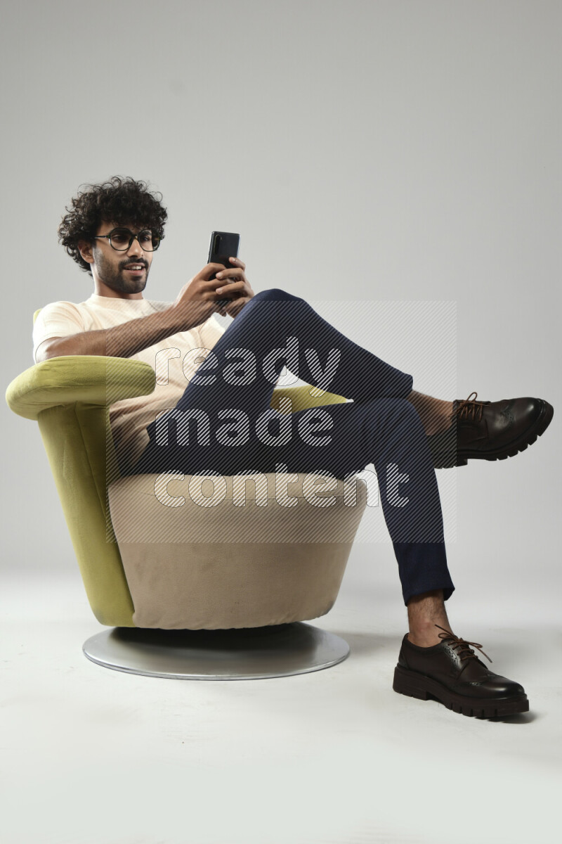 A man wearing casual sitting on a chair texting on the phone on white background