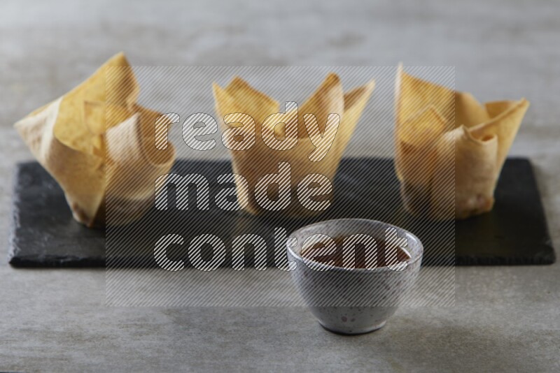 wonton cups with soy sauce ramkin on rectangle slate on grey textured counter top