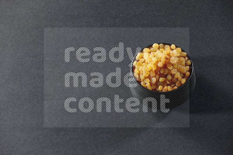 A black pottery bowl full of raisins on a black background in different angles