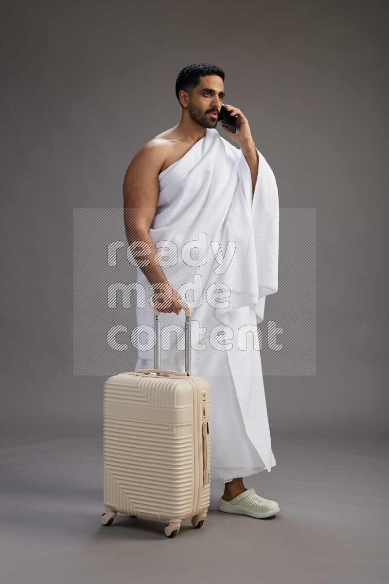 A man wearing Ehram Standing holding traveling bag on gray background