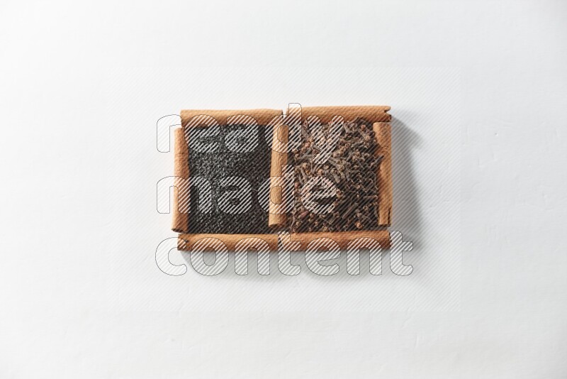 رمربعان من أعواد القرفة ممتلئان بالقرنفل وحبة البركة السوداء علي خلفية بيضاء