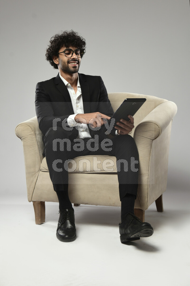 A man wearing formal sitting on a chair browsing on a tablet on white background