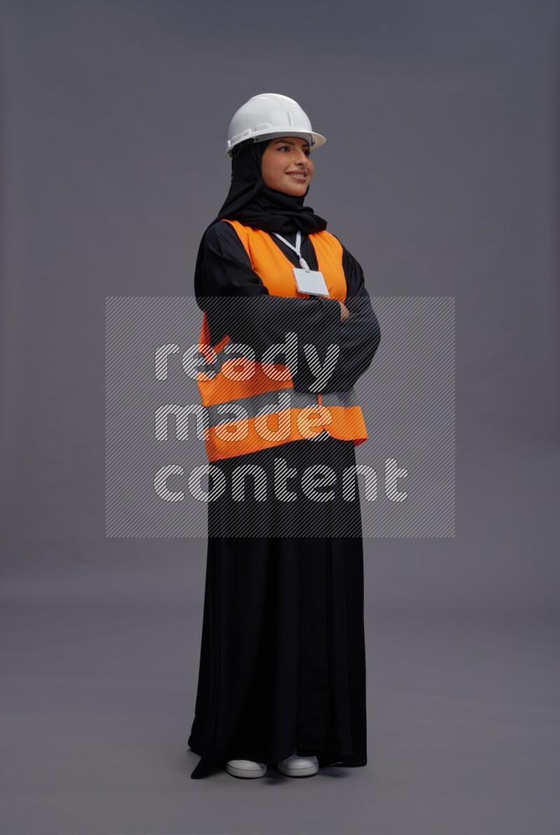 Saudi woman wearing Abaya with engineer vest with neck strap employee badge standing with crossed arms on gray background