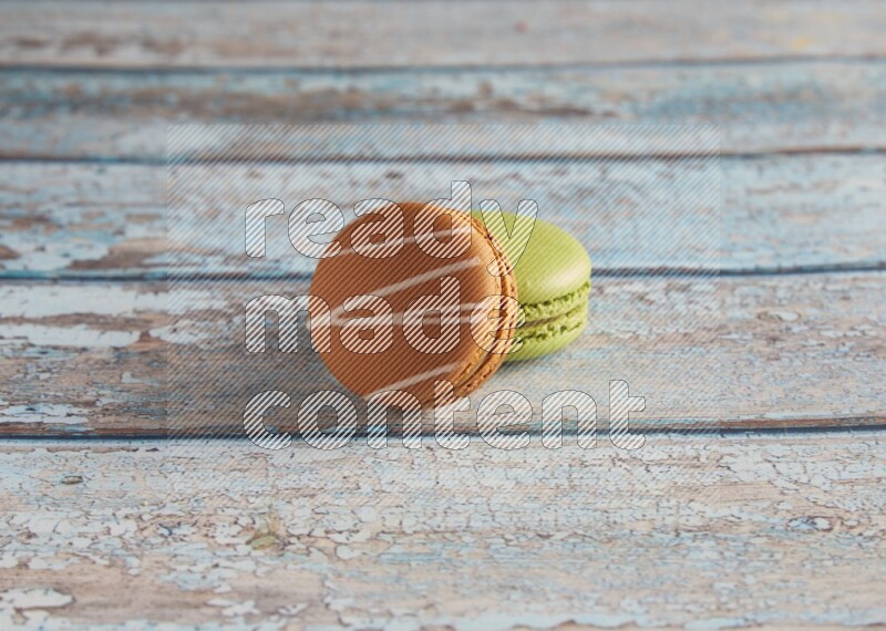 45º Shot of of two assorted Brown Irish Cream, and Green Pistachio macarons  on light blue background
