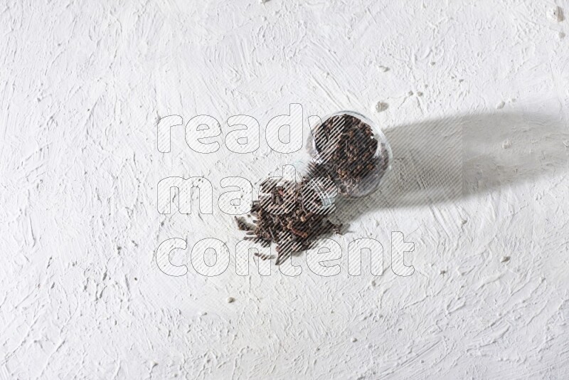 A flipped glass spice jar full of cloves and cloves came out of it on textured white flooring