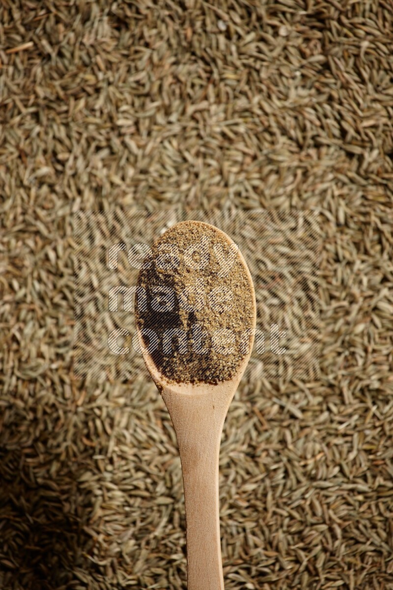 A wooden spoon full of cumin powder on a cumin seeds background