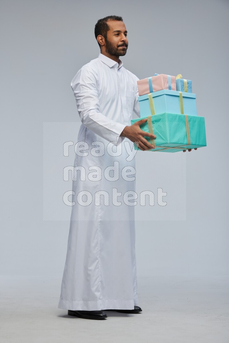 Saudi man Wearing thob standing holding gift box on Gray background