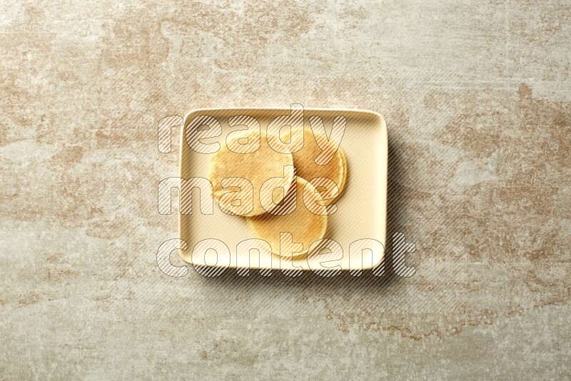 Three stacked plain mini pancakes in a rectangular plate on beige background