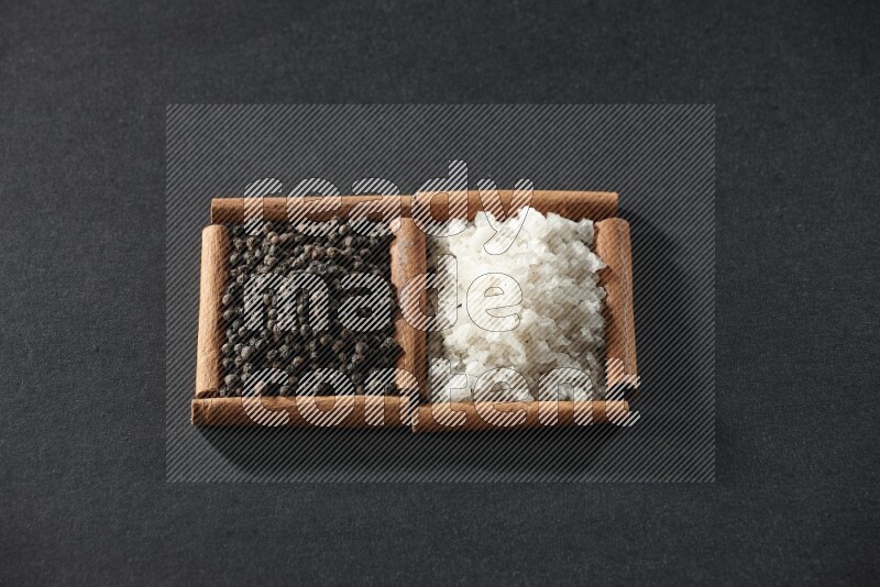 2 squares of cinnamon sticks full of white salt and black peppers on black flooring