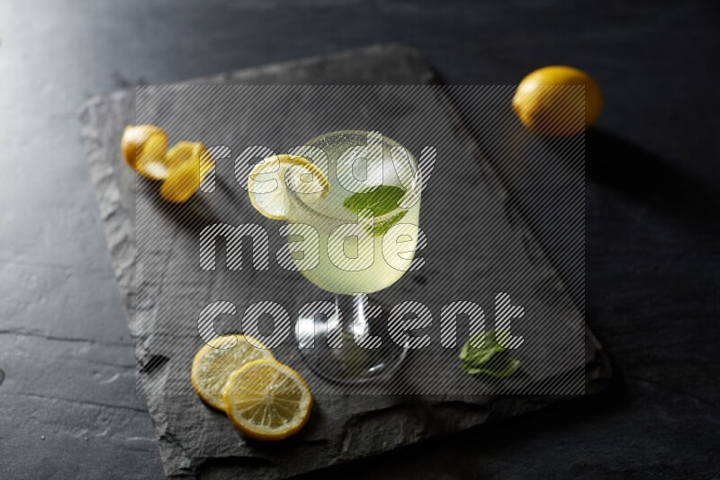 A glass of lemon juice with a lemon slice on black background