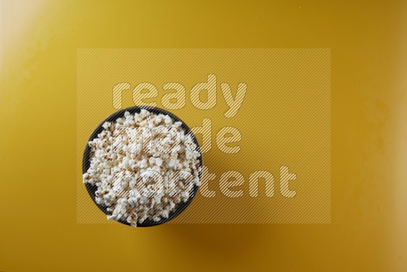 A copper ceramic bowl full of popcorn on a yellow background in different angles