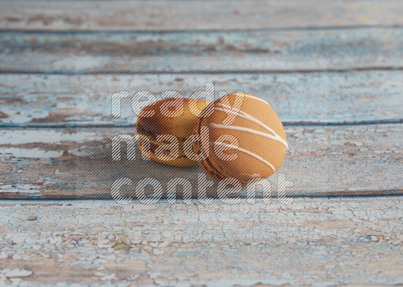 45º Shot of of two assorted Brown Irish Cream, and Yellow Crème Brulée macarons on light blue background