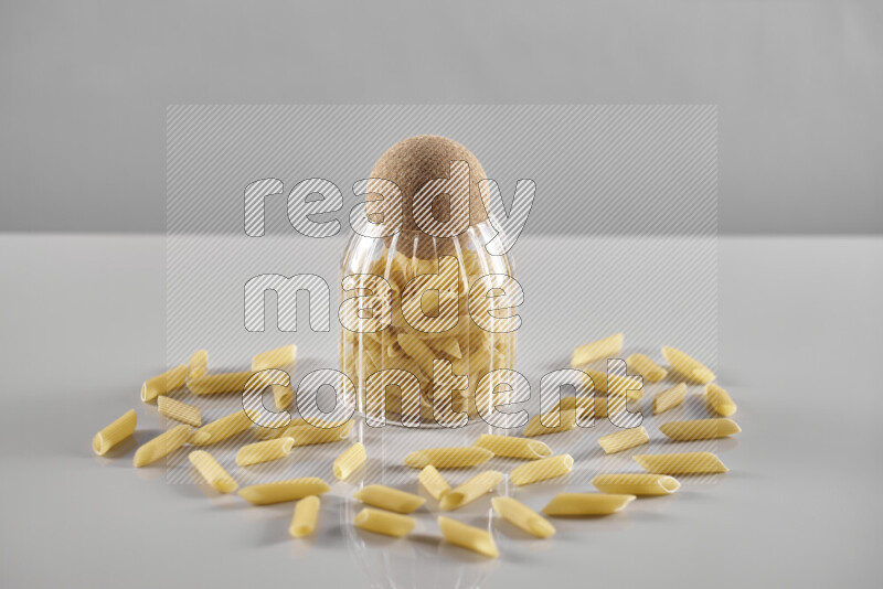 Raw pasta in a glass jar on light grey background