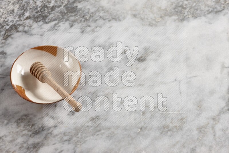 Multicolored pottery plate with wooden honey dipper in it on grey marble background