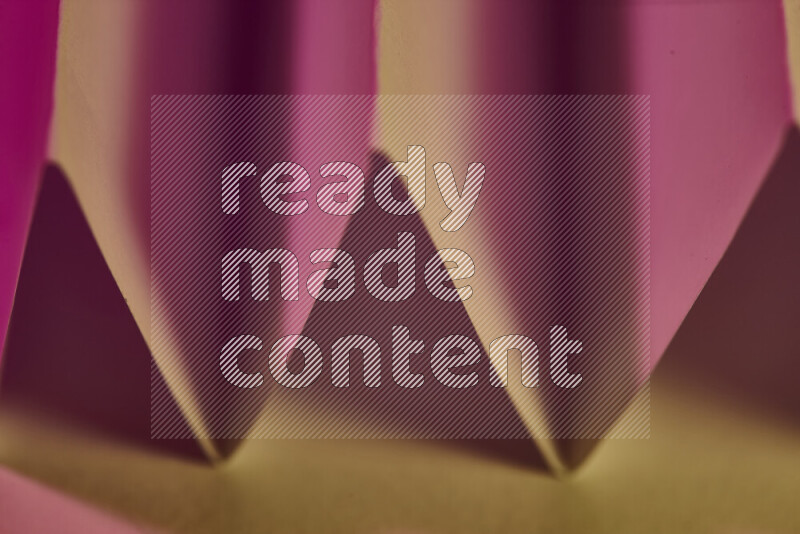 A close-up abstract image showing sharp geometric paper folds in pink gradients and warm tones