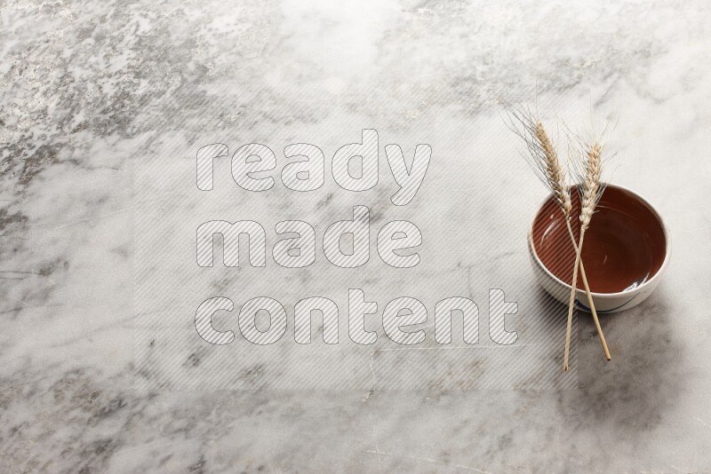 Wheat stalks on brown pottery bowl on grey marble background