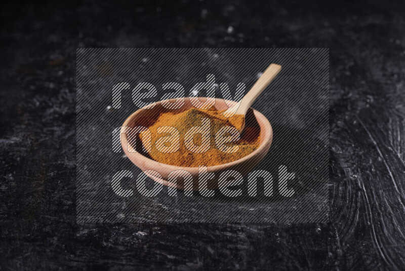 A wooden bowl full of ground paprika powder and a wooden spoon in it on black background