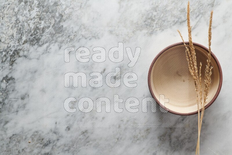 Wheat stalks on beige pottery oven bowl on grey marble background
