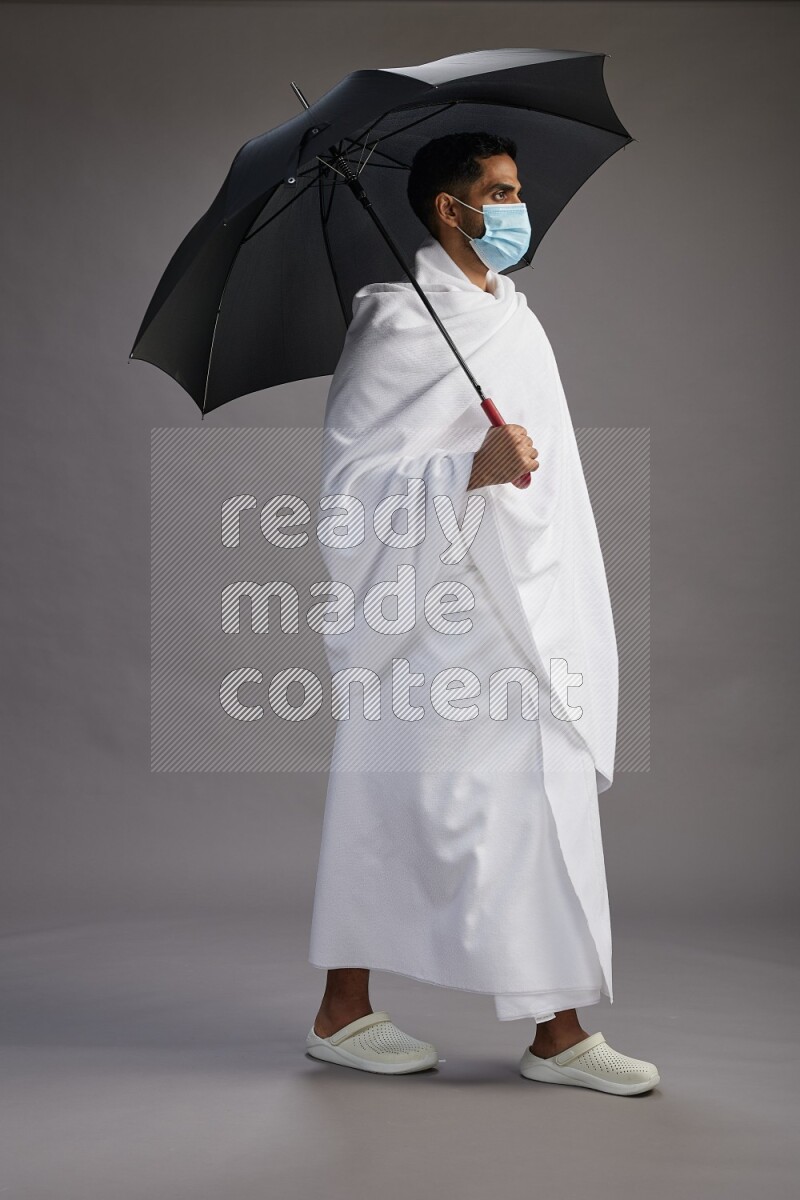 A man wearing Ehram and mask Standing holding umbrella on gray background on gray background
