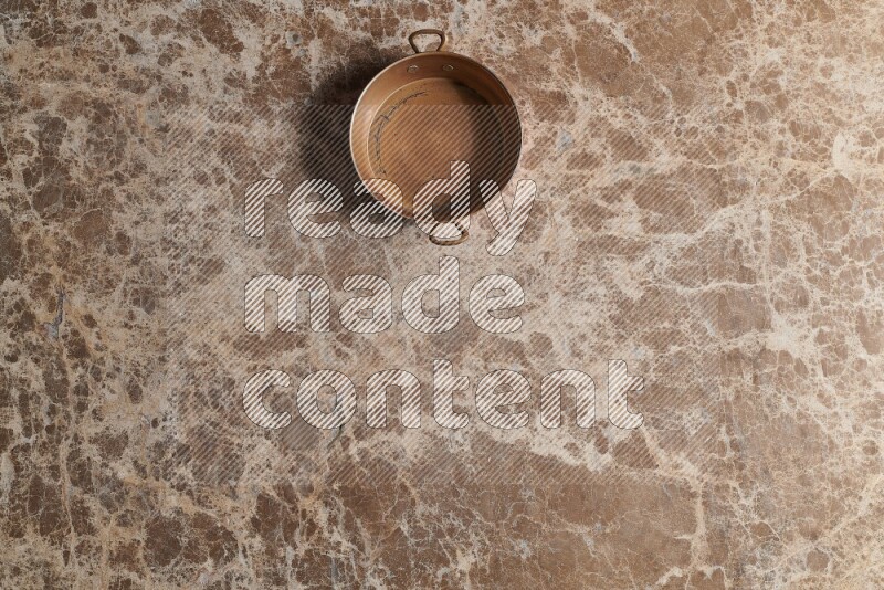 A small copper pan on beige marble background