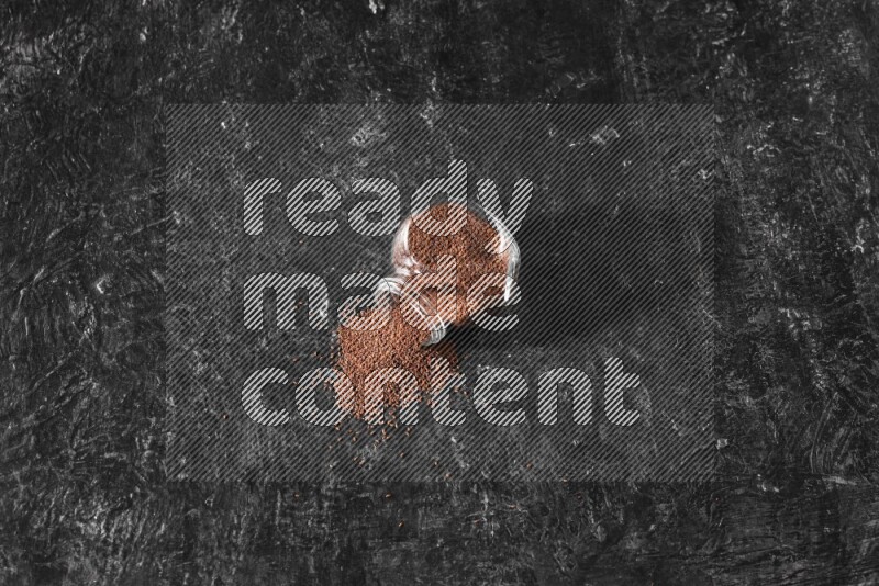 A glass spice jar full of garden cress seeds flipped and seeds spread out a textured black flooring