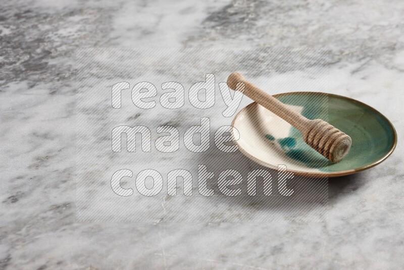 Multicolored pottery plate with wooden honey dipper in it on grey marble background