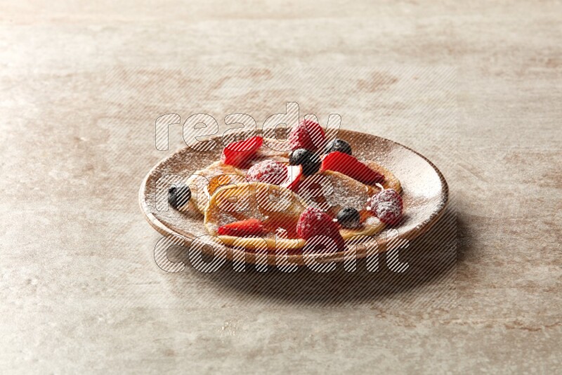 Five stacked mixed berries mini pancakes in a brown plate on beige background