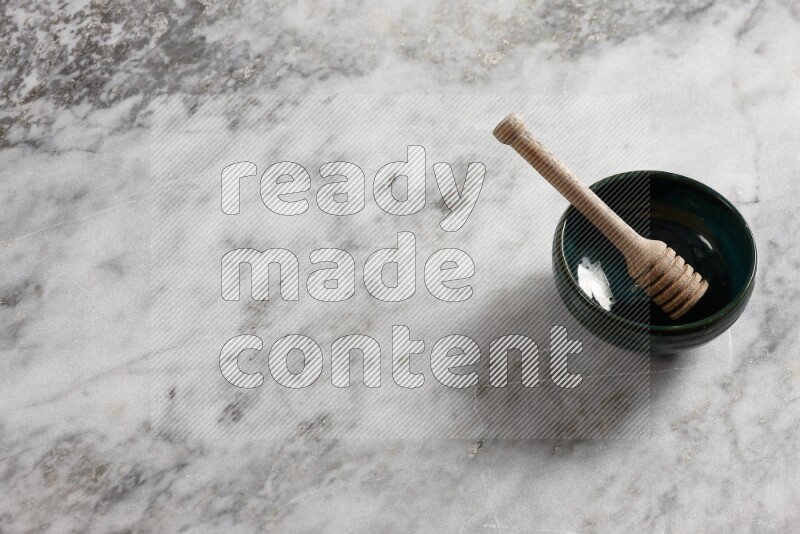 Dark green pottery bowl with wooden honey dipper in it on grey marble background
