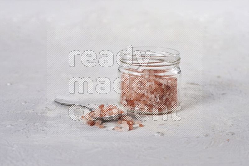 A glass jar full of coarse himalayan salt crystals on white background